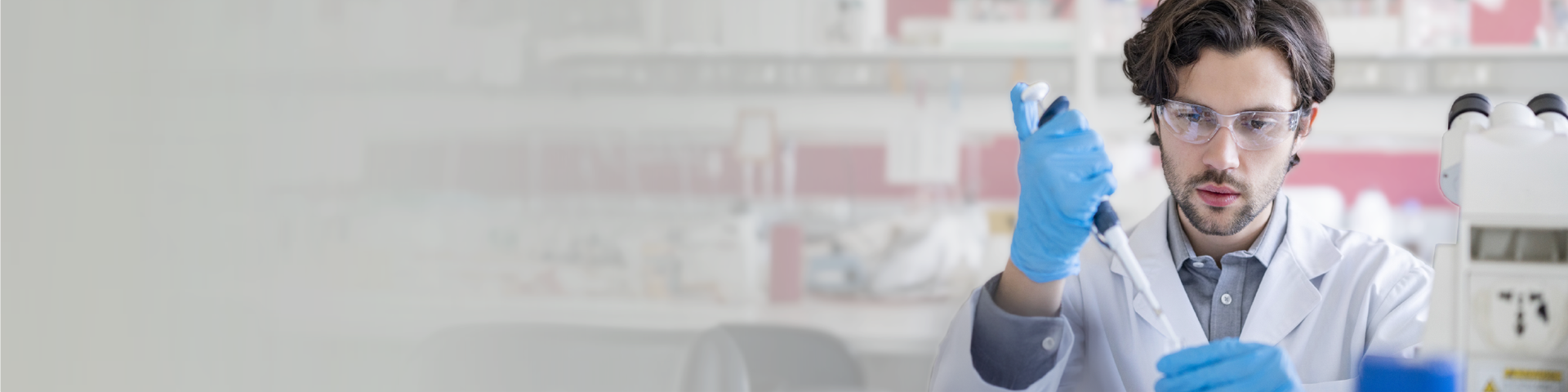 A man wearing a lab coat, safety goggles, and rubber gloves handling chemicals with a micropipette