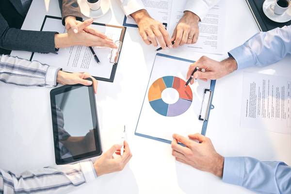People are having a meeting at a desk using a tablet and documents.