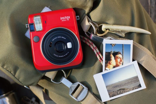 Câmera mini 70 vermelha com duas fotos sobre bolsa verde.