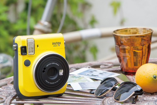 Câmera mini 70 amarelo claro na mesa com óculos de sol, limão e copo