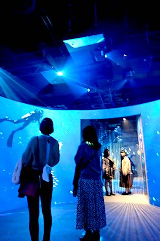 [photo] Two women in foreground and two in background as overhead projects project blue light and image of a scuba diver on walls