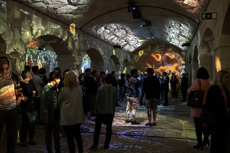 [photo] Crowds of guests inside cathedral-style room and images of stone and brick projected unto walls, floor, and ceiling
