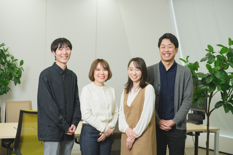 オフィス内で並んで立つ若手エンジニア4名のグループ写真