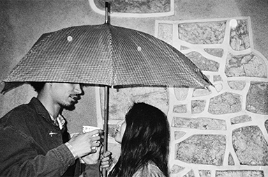 Two people facing each other and talking under an umbrella