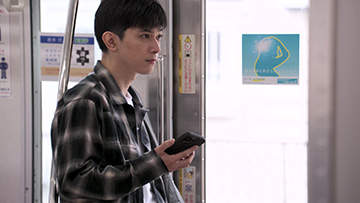 電車の中でスマホを手に持つ吉沢さん