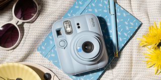 ノートやサングラスとともに布の上に置かれたinstax™ “チェキ”