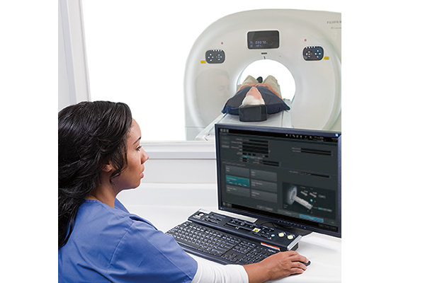 Here is a photo showing a female operator seated at the iStream Focus Edition operator console in the operation room, setting up scanning parameters. The photo also shows an elderly male patient lying on the iStream Focus Edition patient table, waiting before the scan begins.