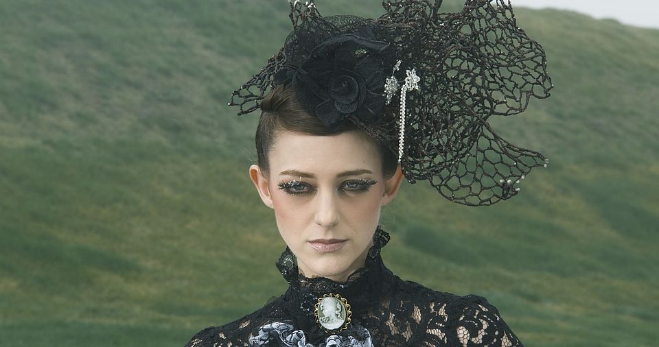 [photo] A face close-up of a lady dressed in a mediaval dress & hat sitting on a green grass on a cloudy day