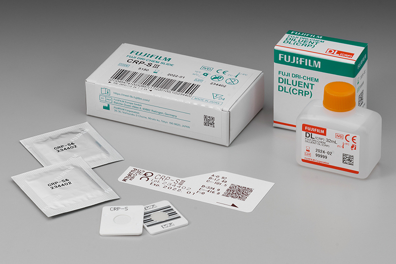 [photo] Box of CRP-SⅢ DRI-CHEM Slides with 2 slides in foil wrapper, 2 slides without packaging (front and back view), and QC card, next to box of Diluent DL (CRP) and bottle of diluent DL