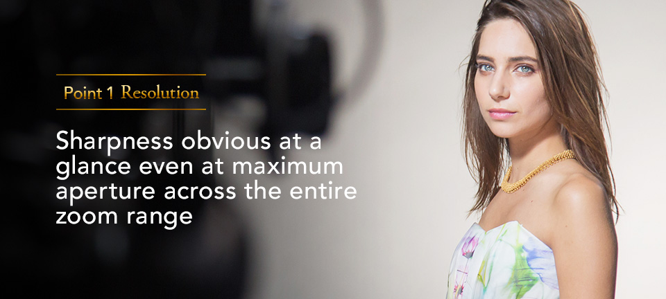 [photo] Point 1 Resolution: Sharpness obvious at a glance even at a maximum aperture across the entire zoom range" text with medium shot a lady staring right at the camera