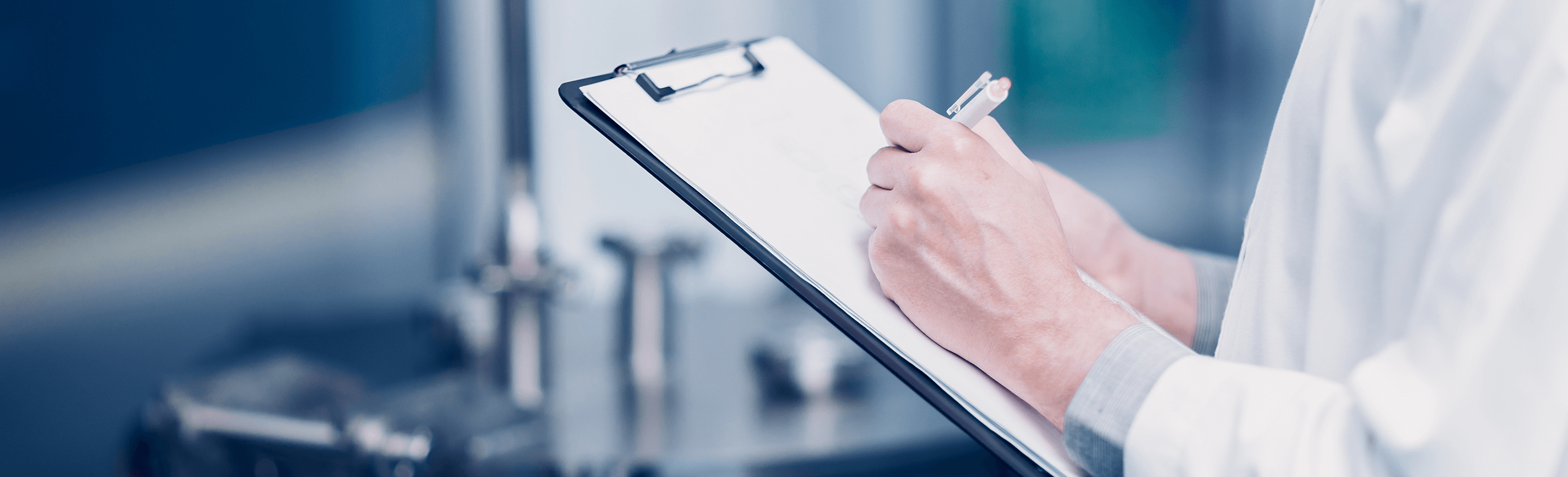 person wearing a lab coat writes on a clipboard