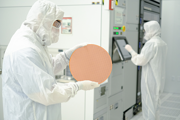 A worker in a clean suit holds a silicon wafer in his hand.