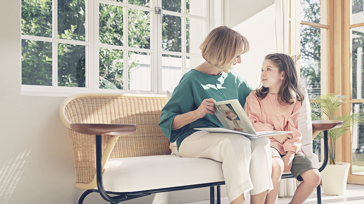 A grandmother and her granddaughter are sitting on a couch. The grandmother opens a photo book and talks to her granddaughter.