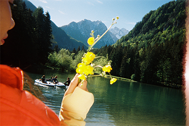 Person by a lakeside holding a flower with a boat in the background