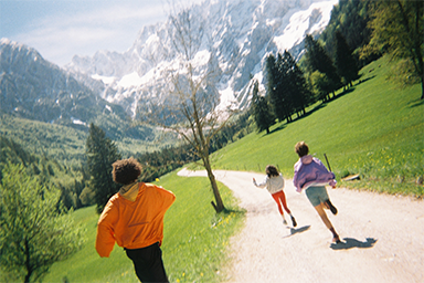 Rear view of three people running down a mountain trail