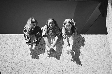 Portrait of three smiling people peeking out from behind a wall